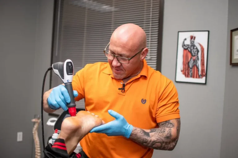 Dr. Tim Ballitch using a shockwave therapy handpiece on the bottom of a patient's foot at Muscle Chiropractic