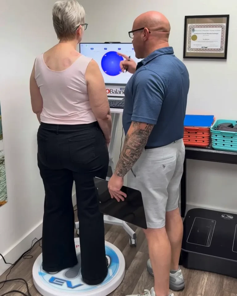 Patient standing on the ProBalance plate while Dr. Tim Ballitch points to the on-screen balance target during balance therapy